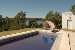 A swimming pool with a unique sculpture, surrounded by trees and a view of a lake.
