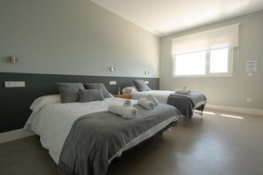 A bedroom with two beds, a window, and a wall-mounted light fixture.