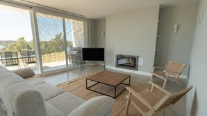 Un salon moderne comprenant un canapé, une table basse, un téléviseur à écran plat, une cheminée et un balcon aménagé avec du mobilier d’extérieur.