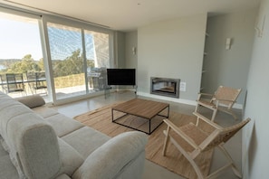 A modern living room with a sofa, a coffee table, a flat-screen TV, a fireplace, and a balcony with outdoor furniture.