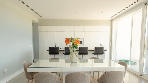 Un espace repas moderne avec une table en verre, quatre chaises et un vase de fleurs.