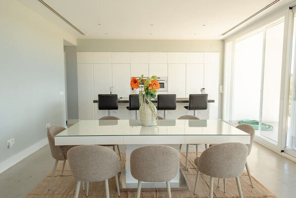 A modern dining area with a glass table, four chairs, and a vase of flowers.