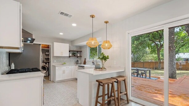 A modern kitchen with white cabinetry, a central island with stools, and a large sliding glass door leading to an outdoor deck. - Near Downtown, 4BR, Austin Heart, Large Backyard (Austin)