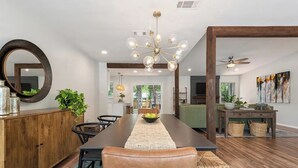 A modern dining room with a long table, chairs, a chandelier, and a wooden cabinet. - Near Downtown, 4BR, Austin Heart, Large Backyard (Austin)
