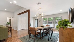 A dining area with a wooden table, chairs, a chandelier, and a view of the outdoors through large windows. - Near Downtown, 4BR, Austin Heart, Large Backyard (Austin)
