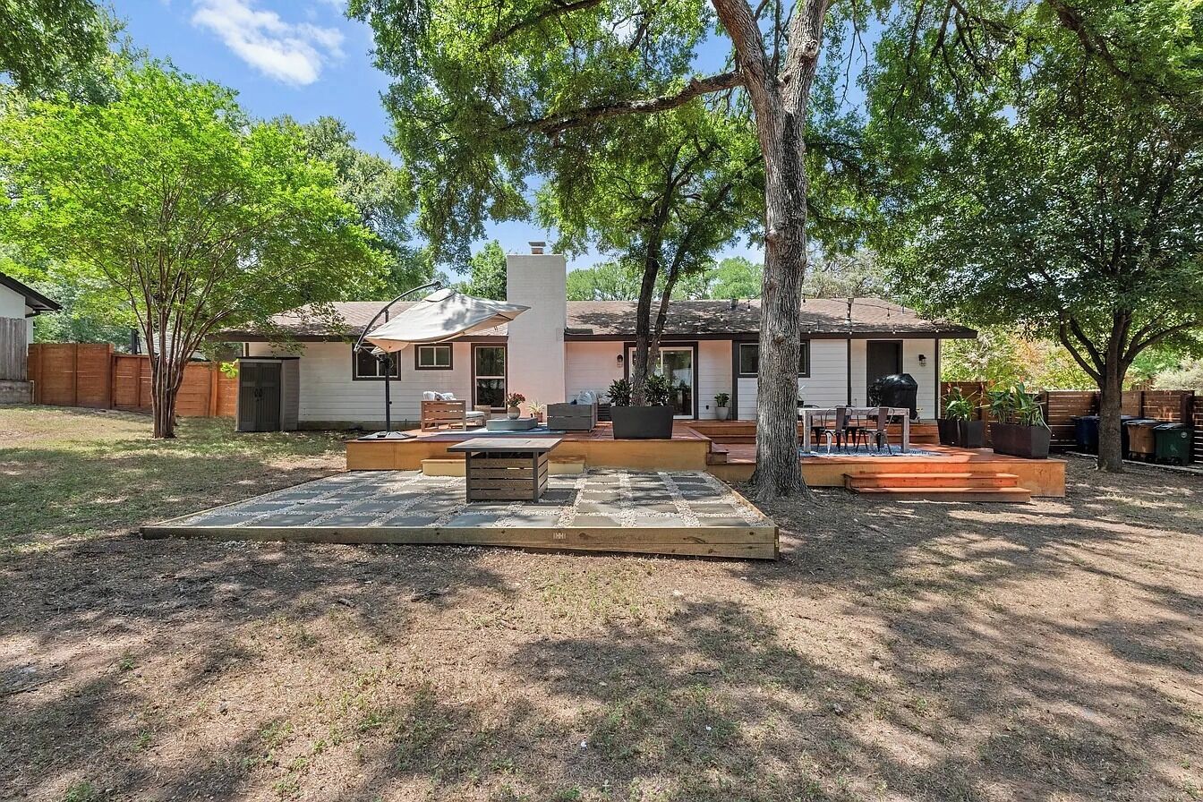A backyard with a patio, a wooden deck, and a house with a chimney.