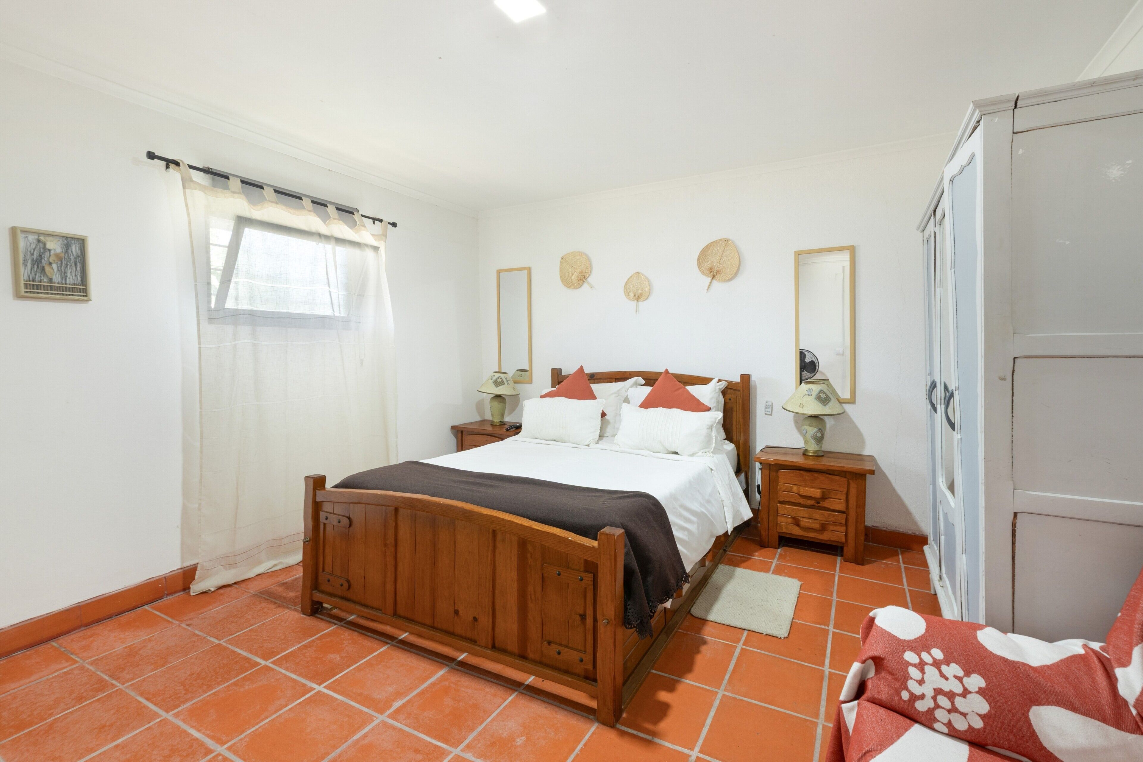 A bedroom with a wooden bed, a nightstand with a lamp, a wardrobe, and a window with curtains.