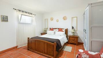 A bedroom with a wooden bed, a nightstand with a lamp, a wardrobe, and a window with curtains.