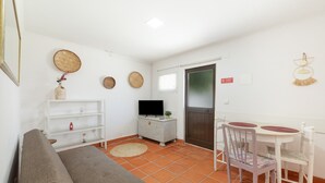 Ein Wohnzimmer mit einer Couch, einem Fernseher, weißen Regalen und einem Esstisch mit Stühlen.