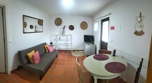 A living room with a sofa, a round table, a television, and decorative wall art.