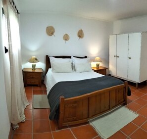 A bedroom with a wooden bed, two bedside tables with lamps, a wardrobe, and a tiled floor.