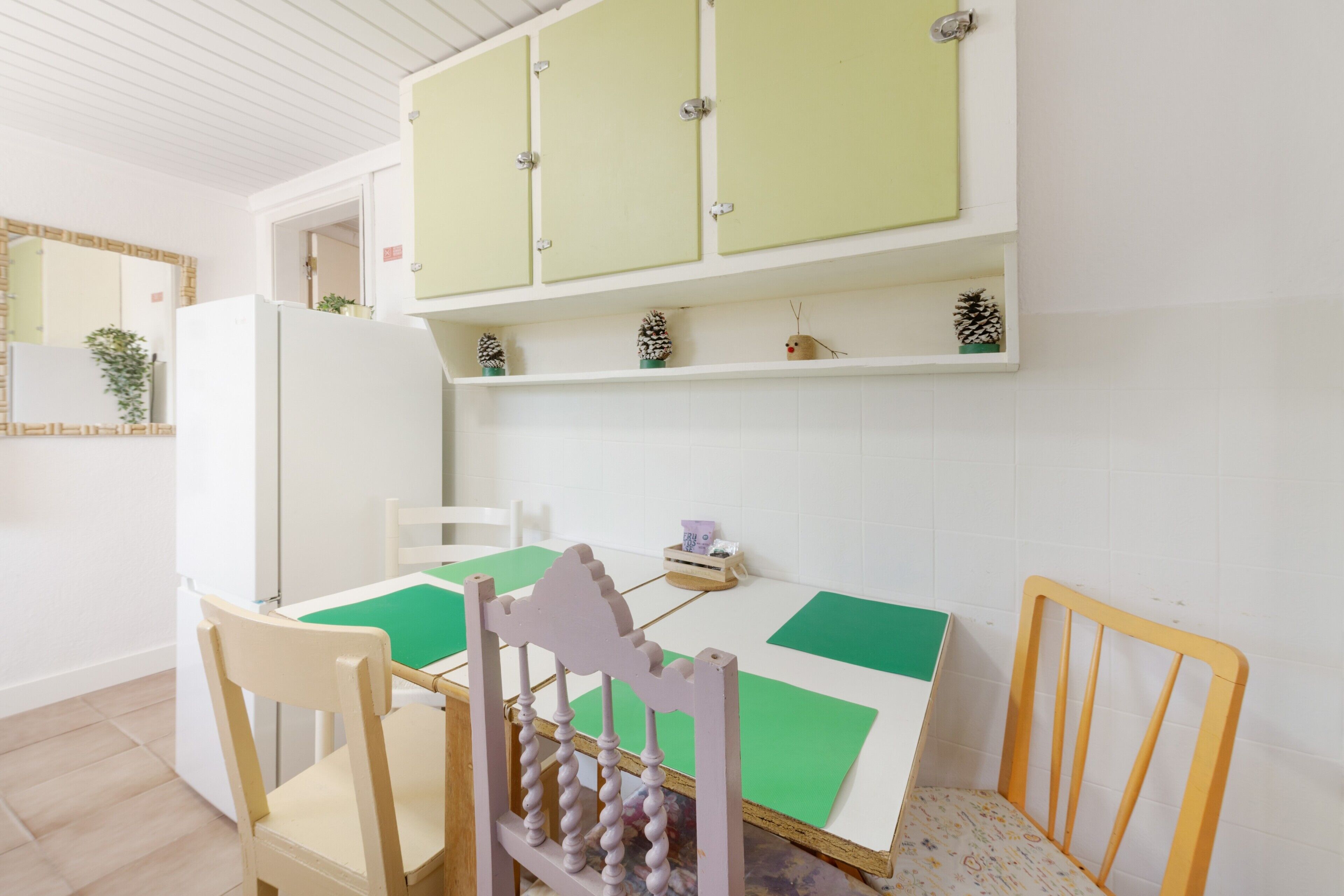 A room with a dining table, chairs, a refrigerator, and a cabinet with decorative items.
