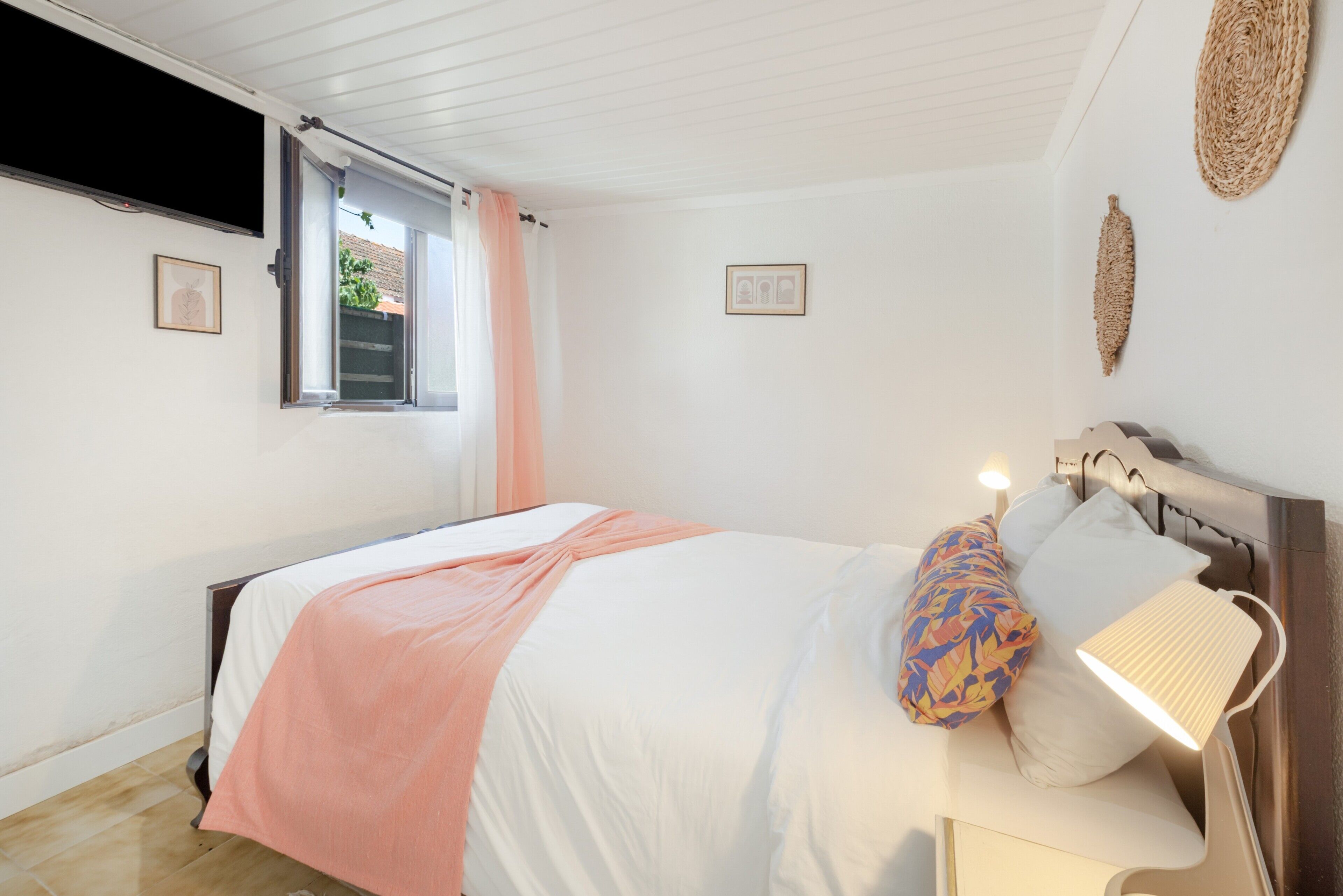A bedroom with a bed, a window with curtains, a bedside lamp, and wall decorations.