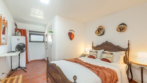 A bedroom with a wooden bed, white bedding, a desk with a fan, a small table with a lamp, and a window with curtains. - Vila Natura – Secret Retreat S2 with Shared Terrace & Garden, Wi-Fi (Santo António da Charneca)
