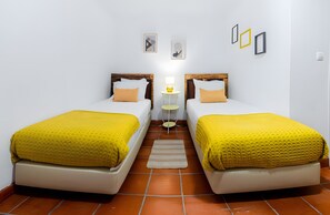 A room with two beds, a small table with a lamp, and a rug on the floor.