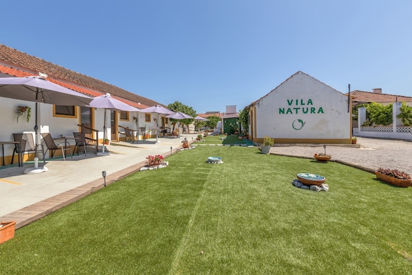 A courtyard with outdoor seating, a sign reading 'Vila Natura,' and a well-maintained lawn.