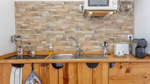 A kitchen with a stone backsplash, a microwave, a sink, and a coffee maker.