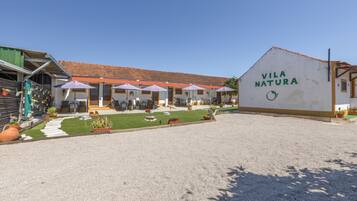 A building with a sign reading 'VILA NATURA' and a covered outdoor seating area with umbrellas.