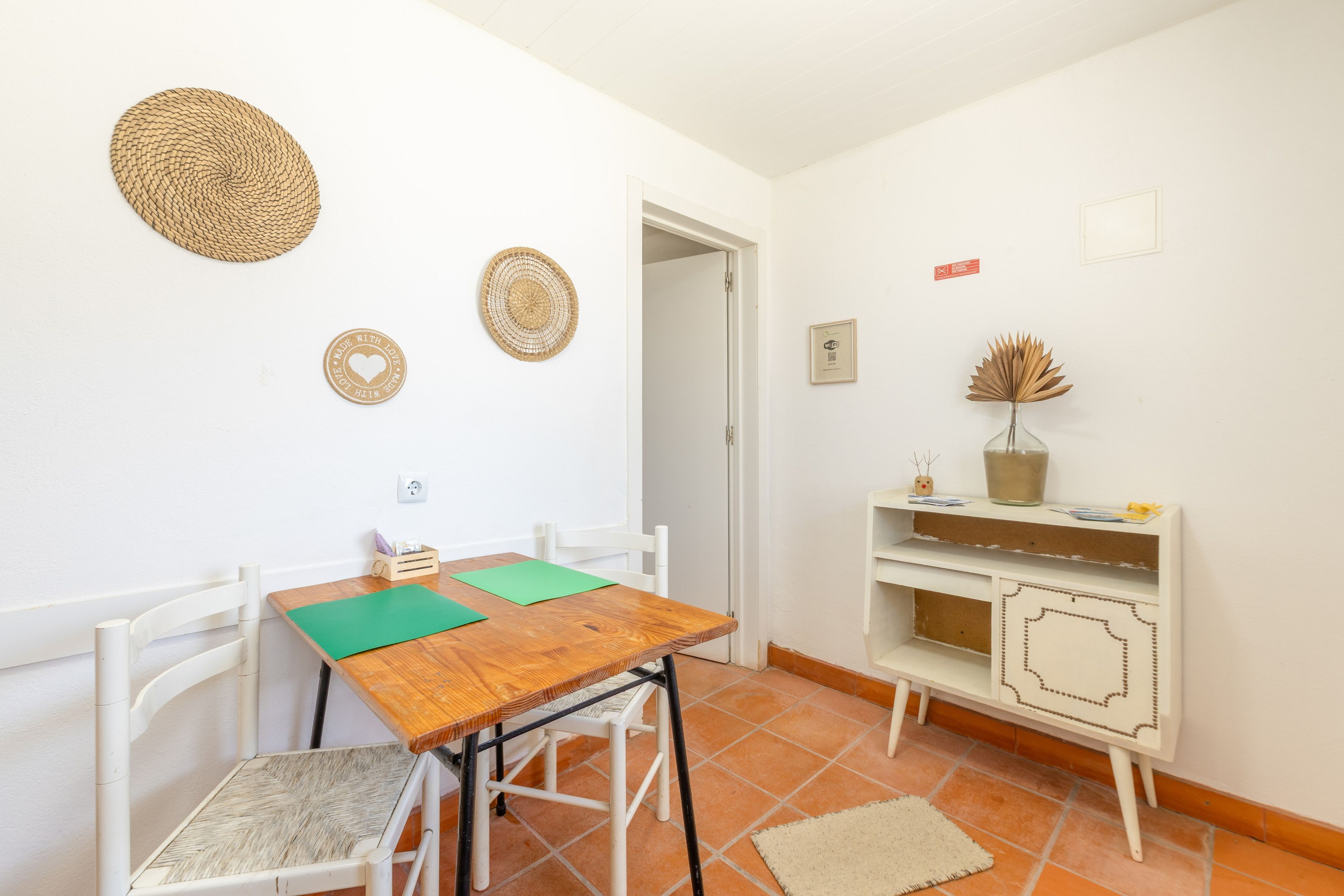 Een kleine, schone kamer met een houten tafel, twee stoelen, een witte kast en een deur naar een andere kamer.