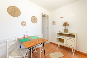 Una habitación pequeña y limpia con una mesa de madera, dos sillas, un armario blanco y una puerta que da a otra habitación.