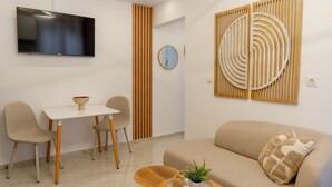 Uma sala de estar moderna com televisão de tela plana, uma mesa de jantar com cadeiras, um sofá com almofada e um painel decorativo na parede.