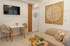 Ein modernes Wohnzimmer mit einem Flachbildfernseher, einem Esstisch mit Stühlen, einer Couch mit Kissen und einer Wandverkleidung.