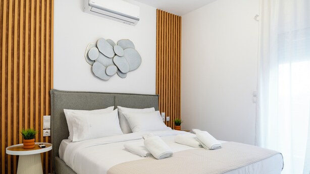 Quarto de hotel moderno com uma cama grande, uma mesinha redonda, ar-condicionado fixado na parede e um objeto decorativo na parede.