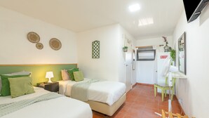 Une chambre d’hôtel avec deux lits, une petite table avec une lampe, un miroir et un ventilateur.