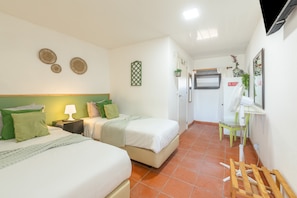Quarto de hotel com duas camas, uma mesinha com abajur, espelho e ventilador.