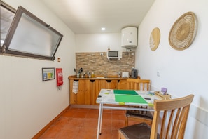 Cozinha compacta equipada com micro-ondas, aquecedor de água e pequena mesa de jantar com cadeiras.