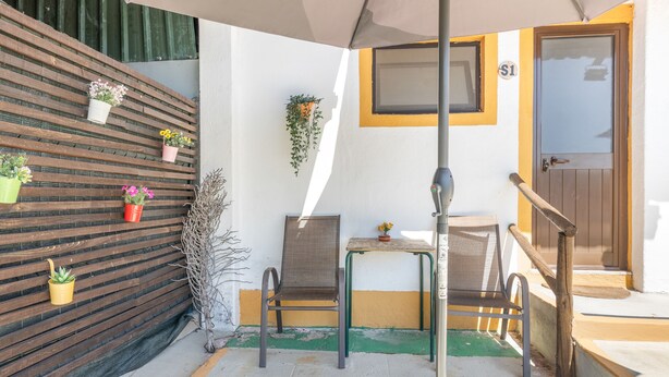 Un petit espace extérieur aménagé avec une table et des chaises, une clôture en bois agrémentée de plantes en pot et une porte avec une plaque numérotée.