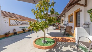 Une cour avec un petit arbre, des sièges extérieurs et un bâtiment doté d’un toit en tuiles et d’une enseigne sur laquelle on peut lire « VILA NATURA ».