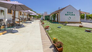 Une cour avec des sièges extérieurs, une pelouse verdoyante et un bâtiment portant l’inscription « Vila Natura ».