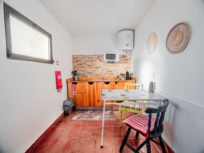 A compact kitchen with a tiled floor, a wooden counter, a small sink, a microwave, and a window.