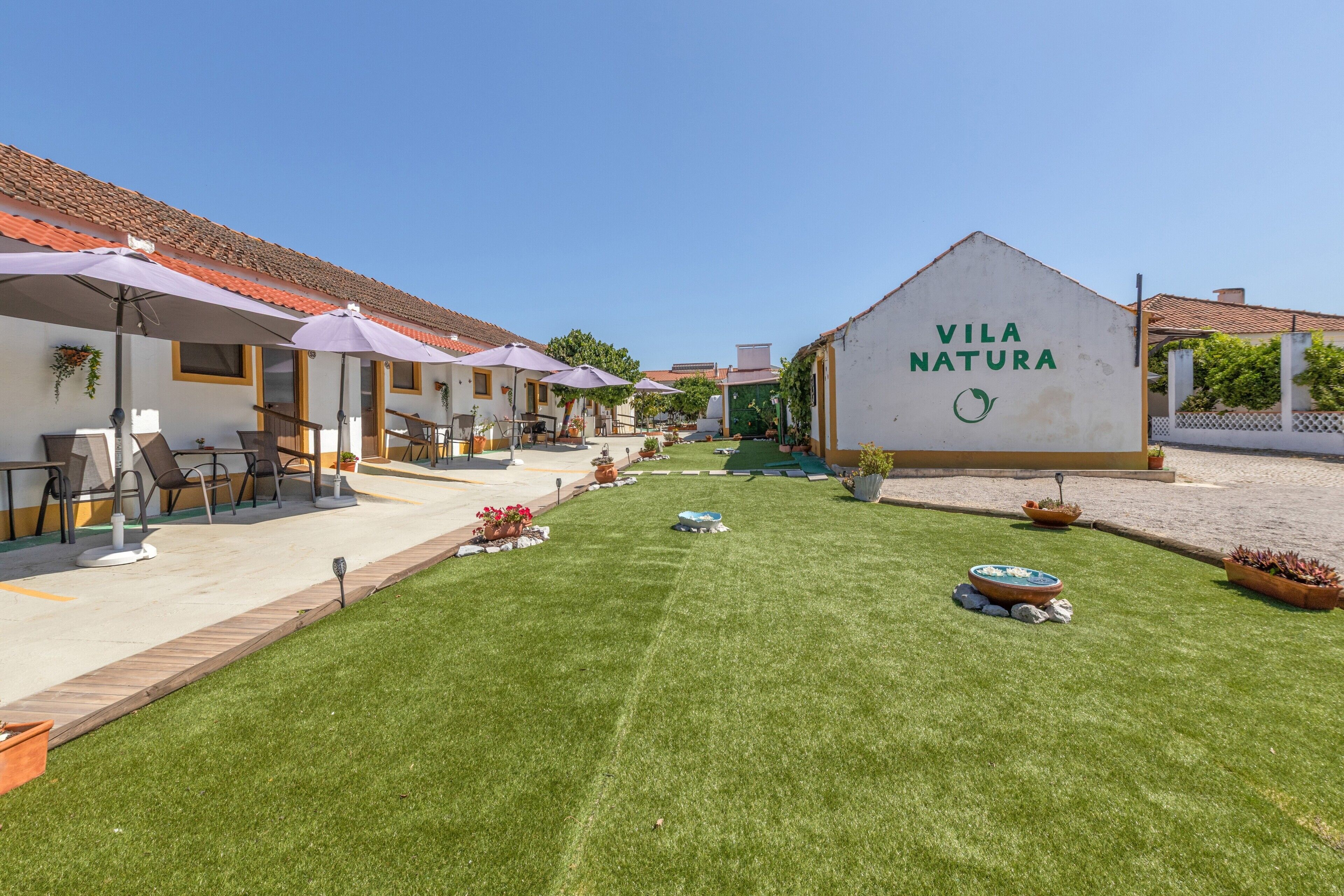 A courtyard with outdoor seating, a sign reading 'Vila Natura,' and a well-maintained lawn.