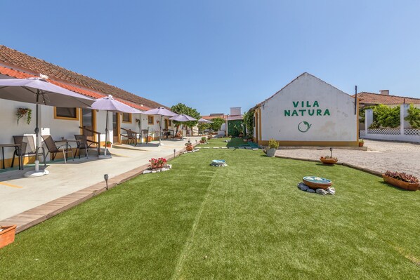 A courtyard with outdoor seating, a sign reading 'Vila Natura,' and a well-maintained lawn.