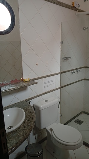 Ein Badezimmer mit Waschbecken, Toilette und Dusche. Ein Schild an der Wand bittet darum, keine Papierhandtücher oder andere Gegenstände in die Toilette zu werfen.