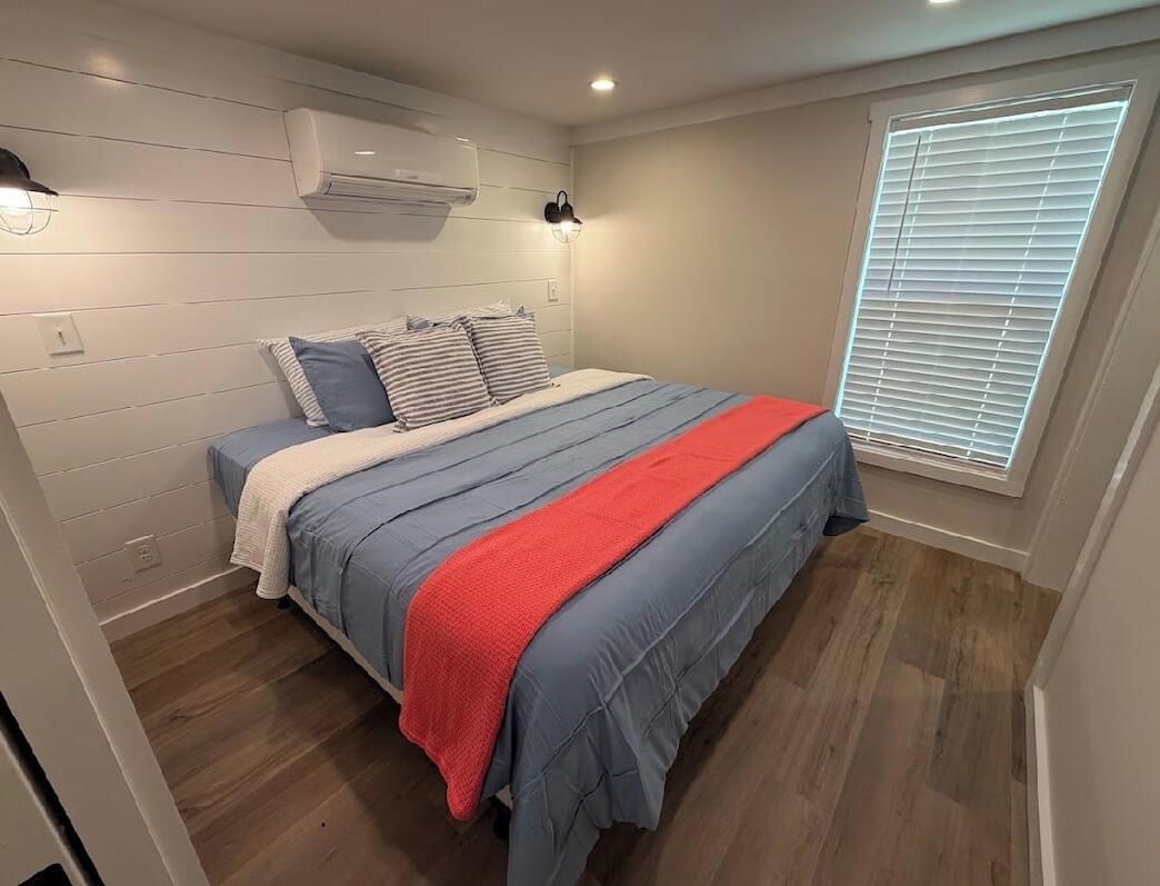 Quarto com cama, janela com persianas e ar condicionado na parede.