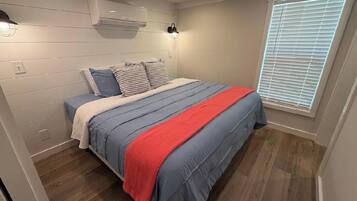 Quarto com cama, janela com persianas e ar condicionado na parede.