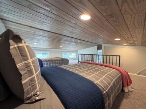 Ein Schlafzimmer mit schrägem Dach, einem Bett mit blauer Decke und einer roten Tagesdecke.