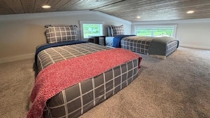Ein Schlafzimmer mit geneigter Decke, zwei Betten mit gemusterten Bettwäsche, einer roten Tagesdecke und einem Teppichboden.
