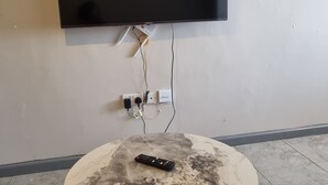 A flat-screen TV mounted on a wall, a remote control on a round table, and a power strip with cables. - Modern Studio in Fedha, Nairobi (Nairobi)