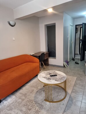 Ein Wohnzimmer mit einer Couch, einem Schreibtisch, einem runden Couchtisch und einer Tür zu einem anderen Raum.