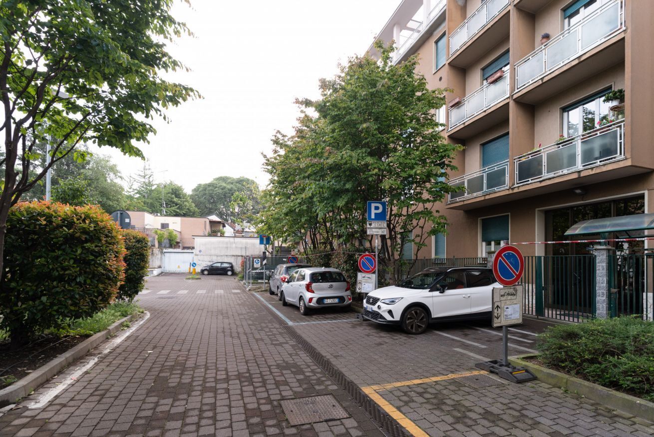 Eine gepflasterte Straße mit parkenden Autos, einem blauen Parkschild und einem Verbotsschild für das Parken.