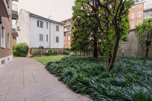 Ein gepflasterter Weg führt zu einem Gebäude mit weißer Fassade und einem von Bäumen gesäumten Garten.
