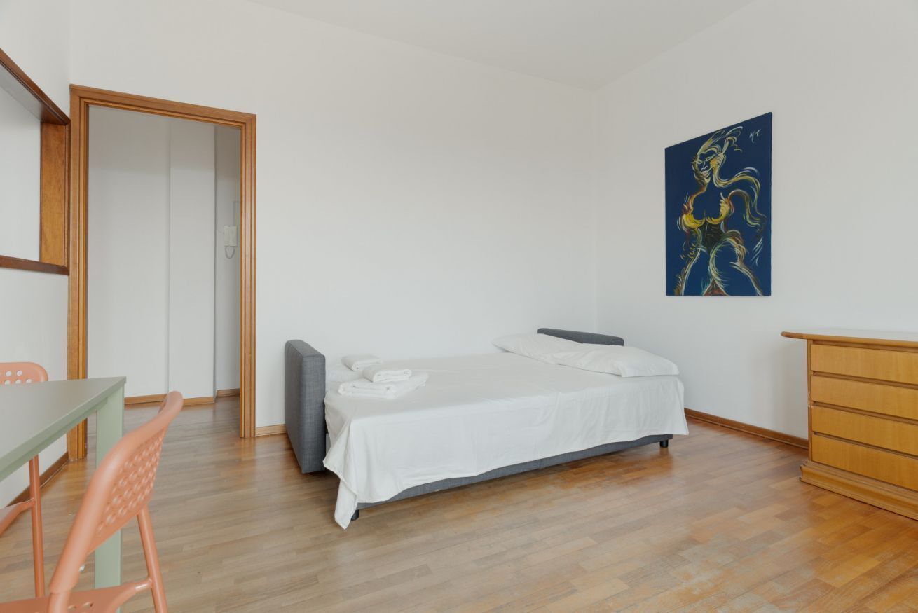 Un dormitorio con cama, escritorio, silla, cómoda y un cuadro en la pared.