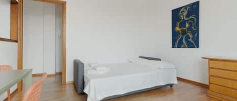 Un dormitorio con cama, escritorio, silla, cómoda y un cuadro en la pared.