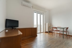 Habitación con una televisión sobre un mueble de madera, una mesa de comedor con sillas y un ventanal corredero que da a un balcón.