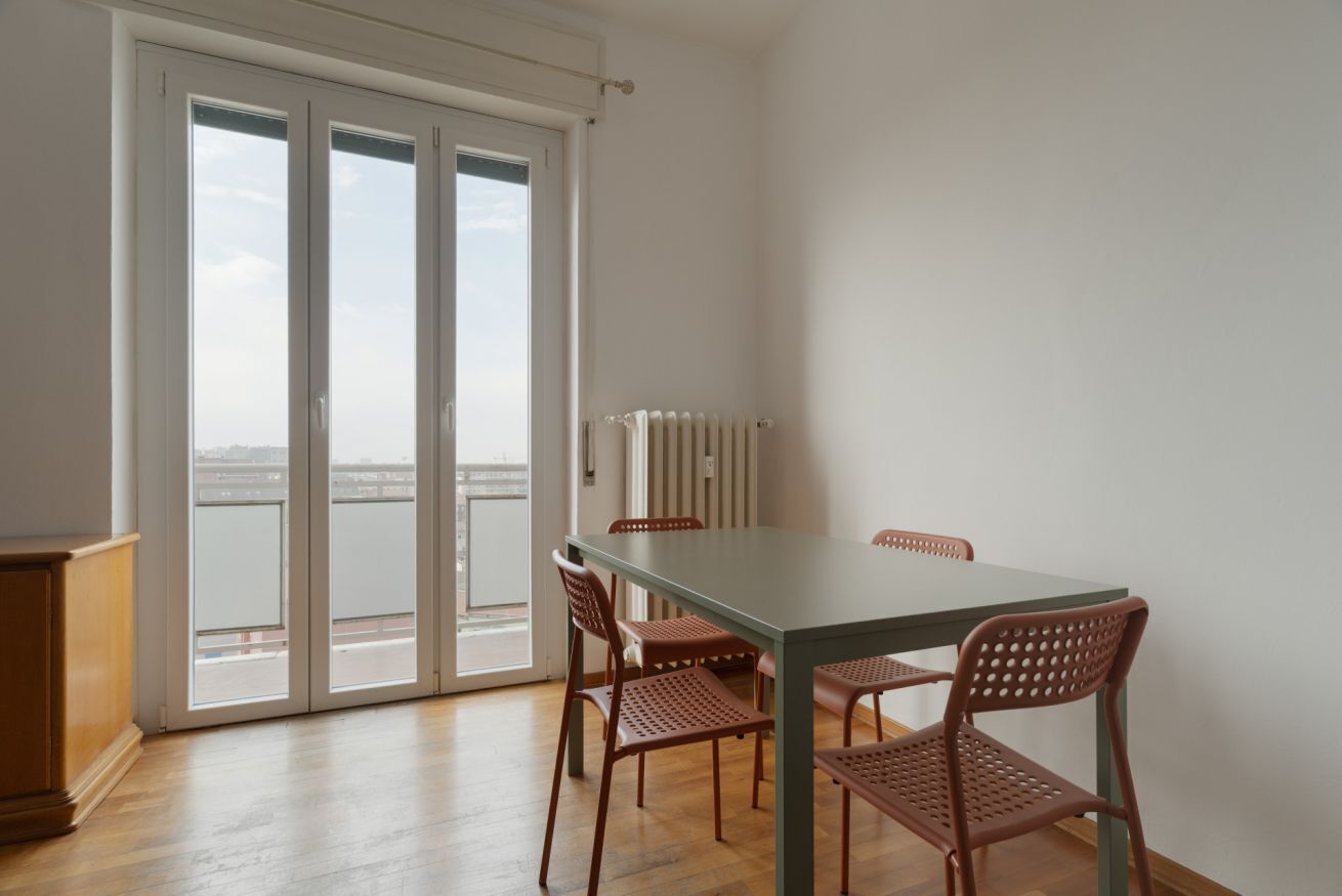 A dining area with a table and chairs, a radiator, and a view through a glass door.