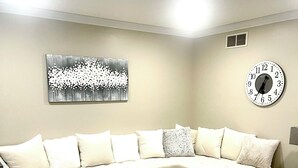 Een woonkamer met een modulaire bank, een rond poef, een klok aan de muur en een abstract kunstwerk.